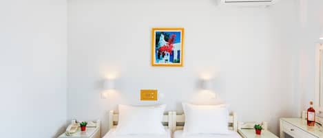 Hotellihuone, jossa on kaksi sänkyä, yöpöydät, pieni työpöytä, peili, ilmastointilaite ja taulu seinällä.