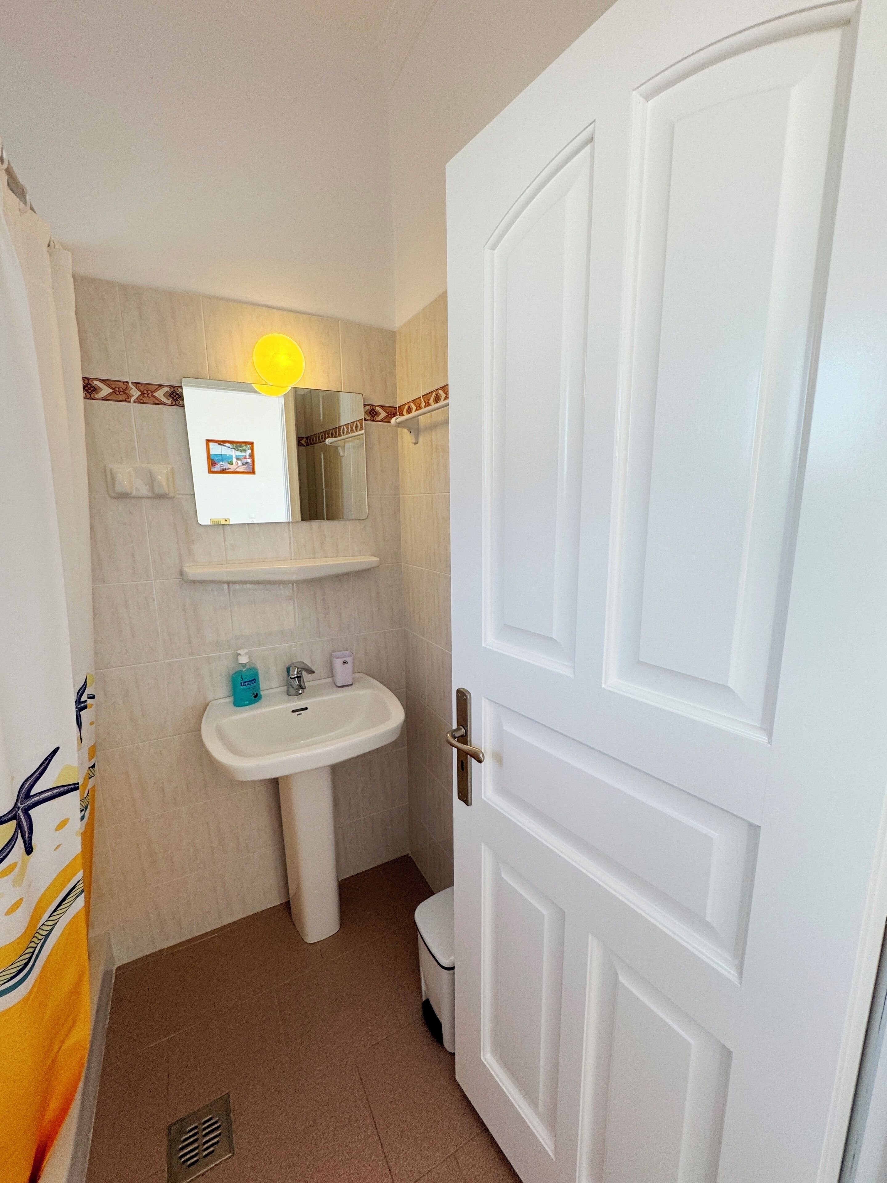Une salle de bain avec un lavabo blanc, un miroir et une porte.
