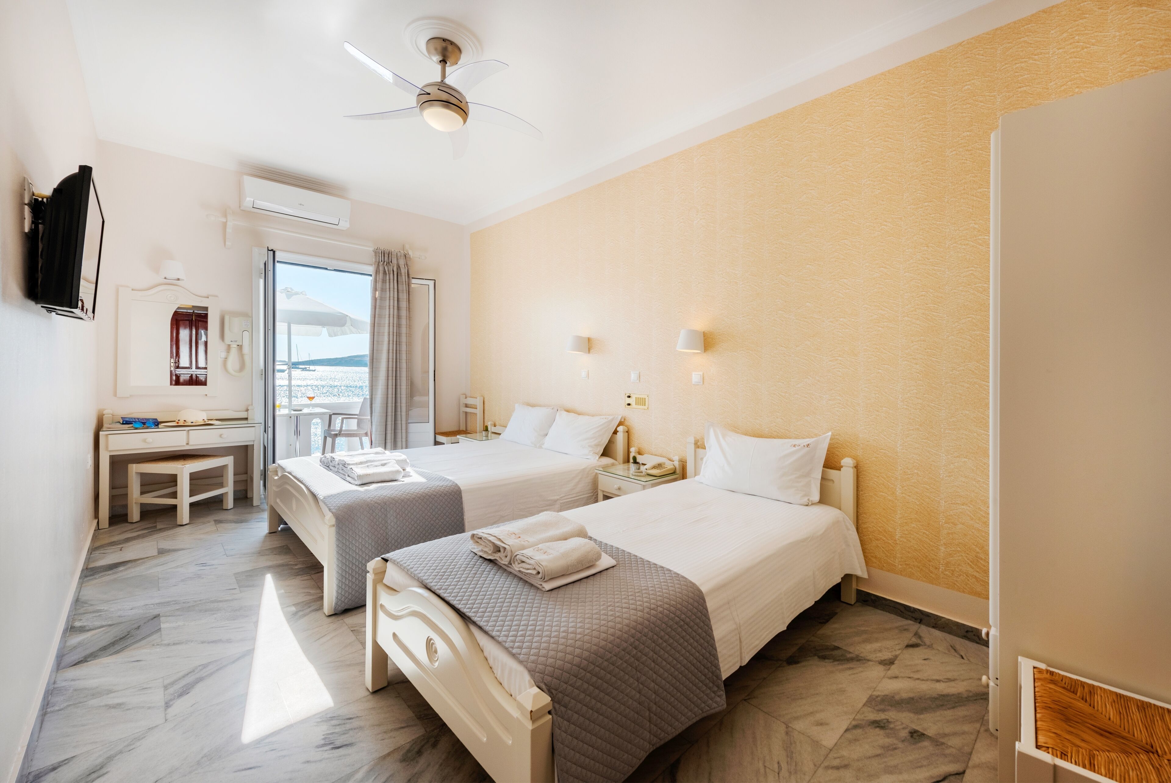 Ein Hotelzimmer mit zwei Betten, einem Schreibtisch, einem Sessel und Meerblick sowie einer Klimaanlage.