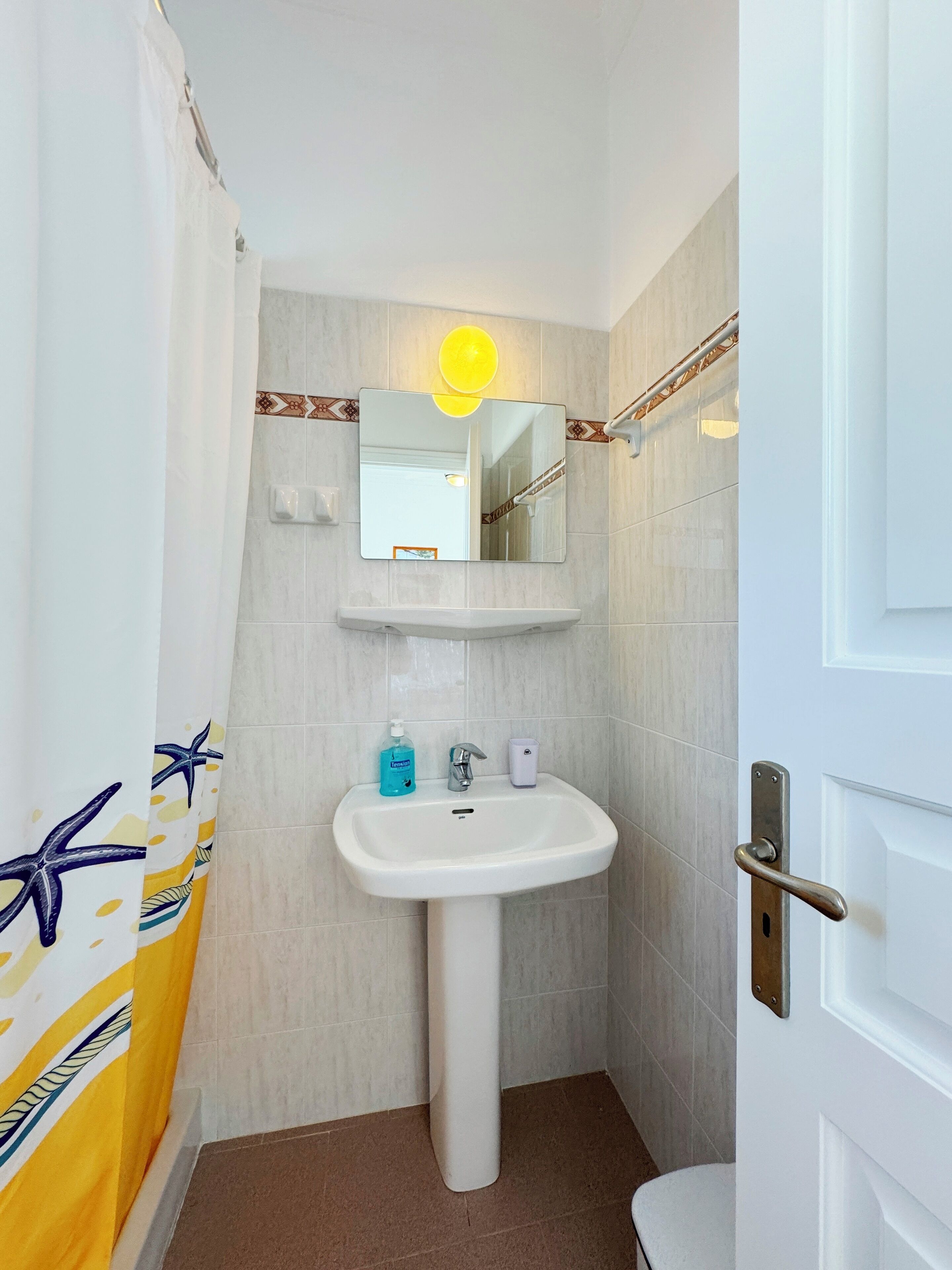 A bathroom with a white sink, a mirror, and a shower curtain with a starfish pattern.