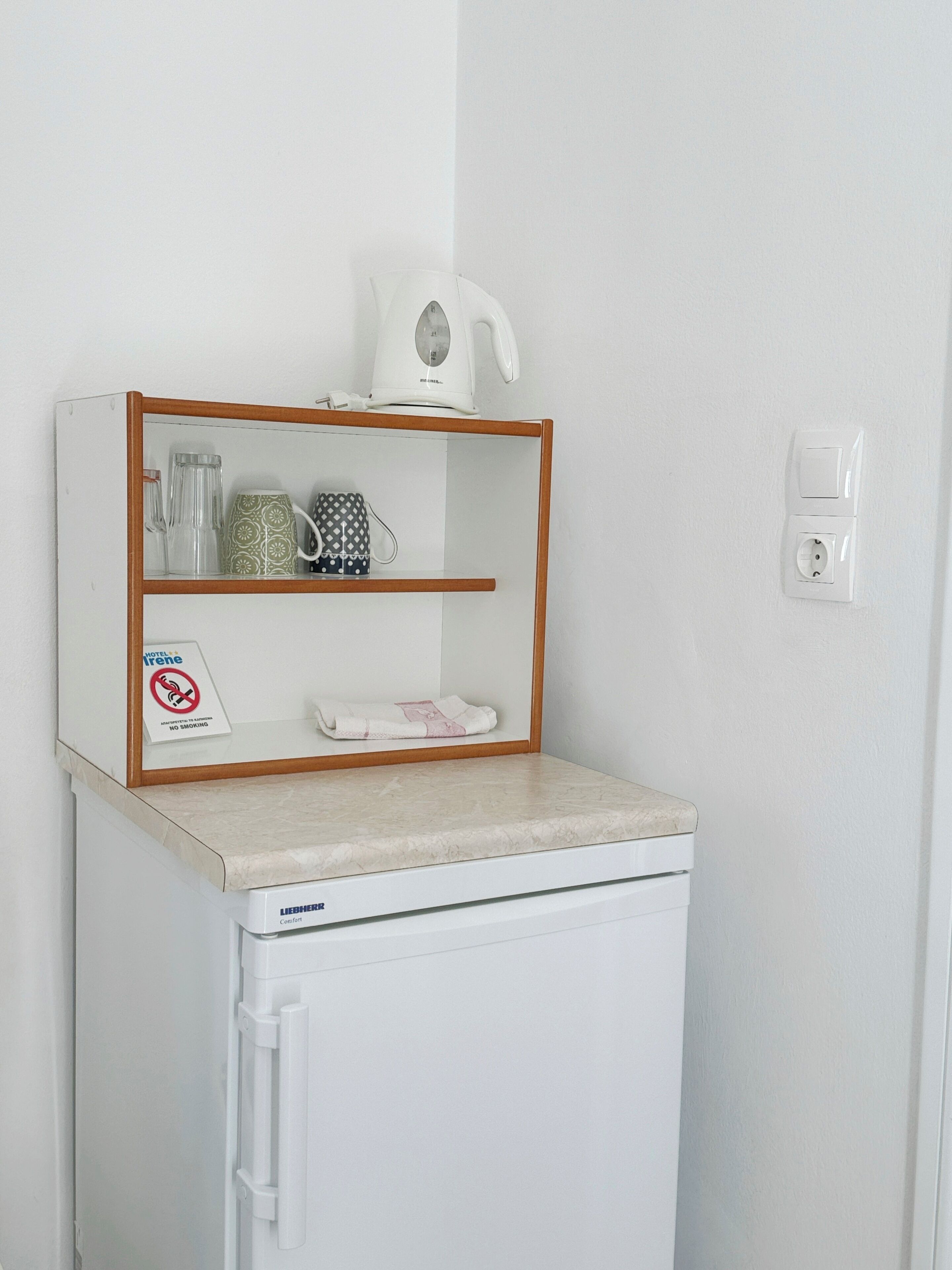 Une petite cuisine équipée d’un réfrigérateur, d’une machine à café, d’une bouilloire et d’un panneau indiquant qu’il est interdit de fumer.