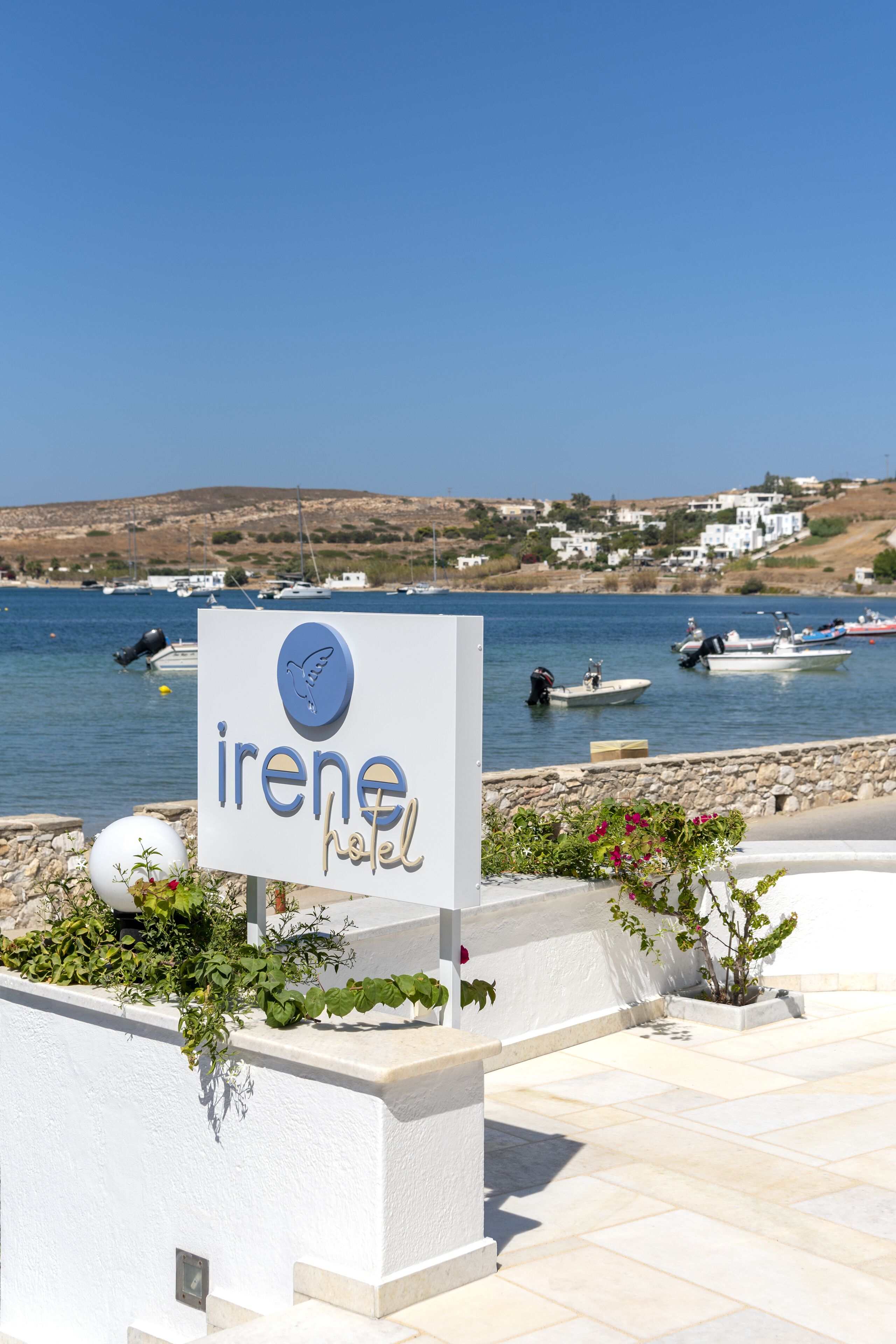 A sign for 'Irene Hotel' with a view of boats on water and houses in the background.