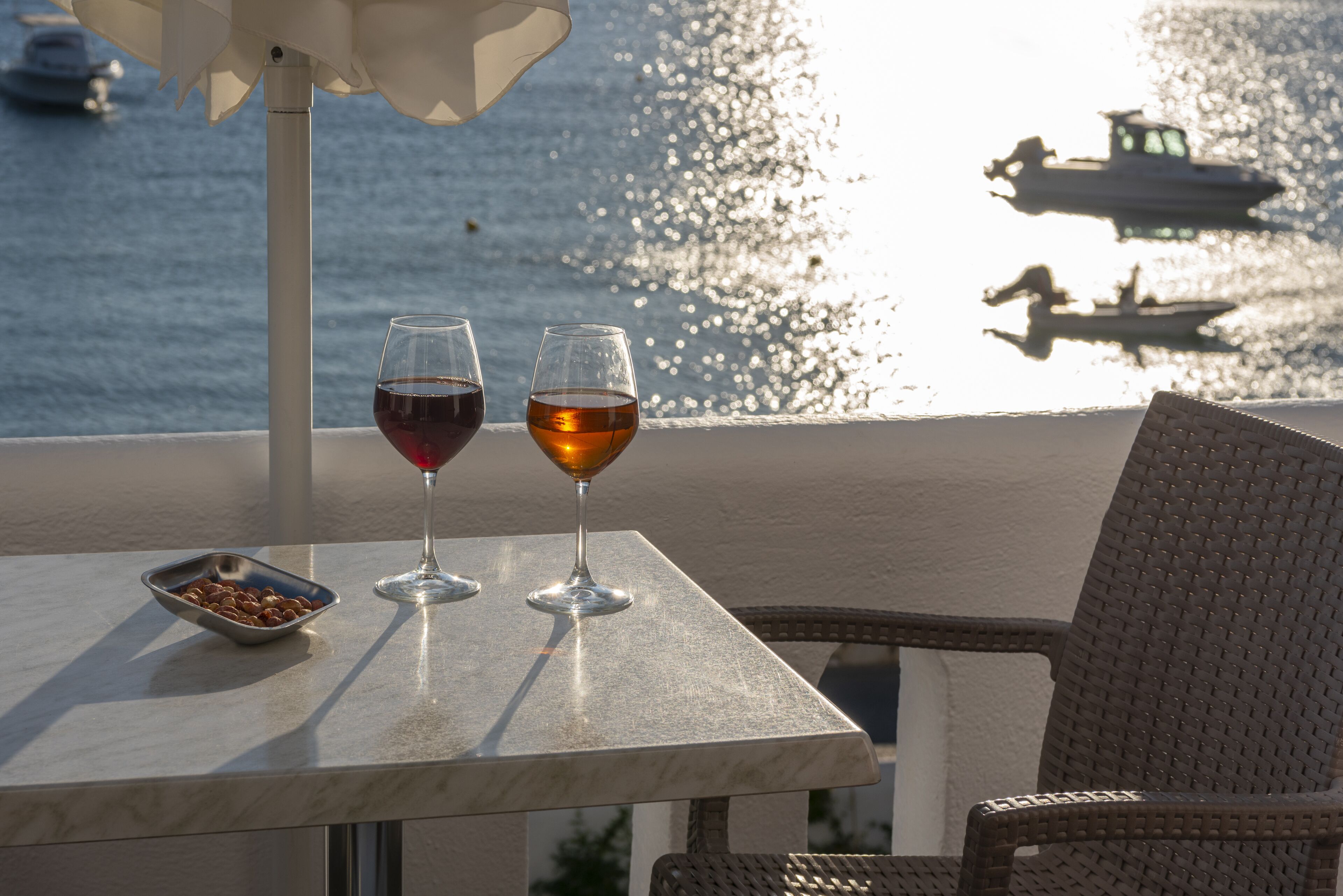 Une table avec deux verres à vin et un bol de noix, donnant sur une étendue d’eau où se trouvent des bateaux.