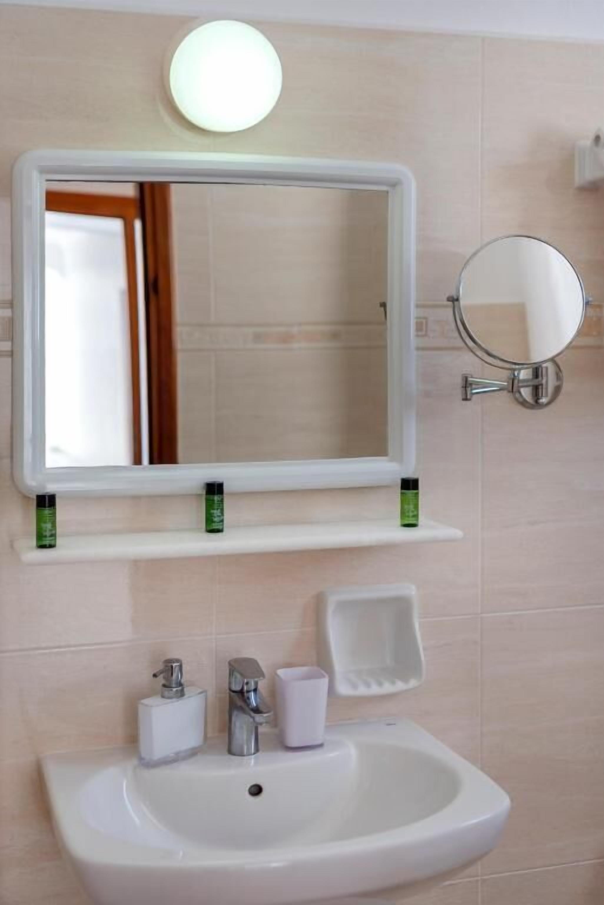 Un baño con un lavamanos blanco, un espejo y un espejo redondo en la pared.