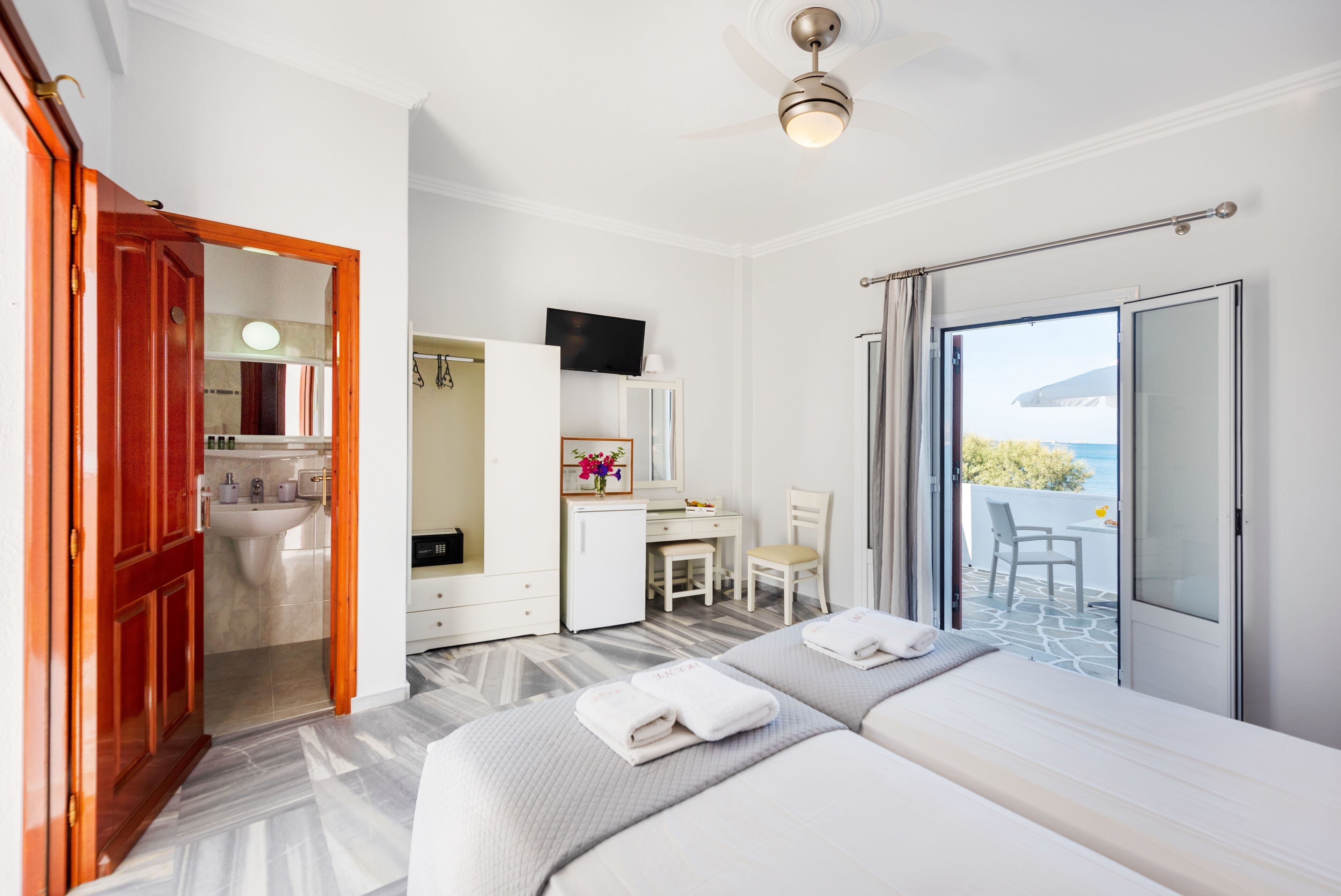 A hotel room with two beds, a desk, a chair, a TV, and a balcony with a view.