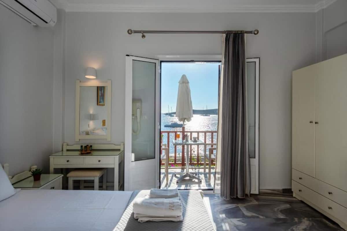 Habitación de hotel con cama, escritorio, espejo y vista al mar desde una puerta abierta.