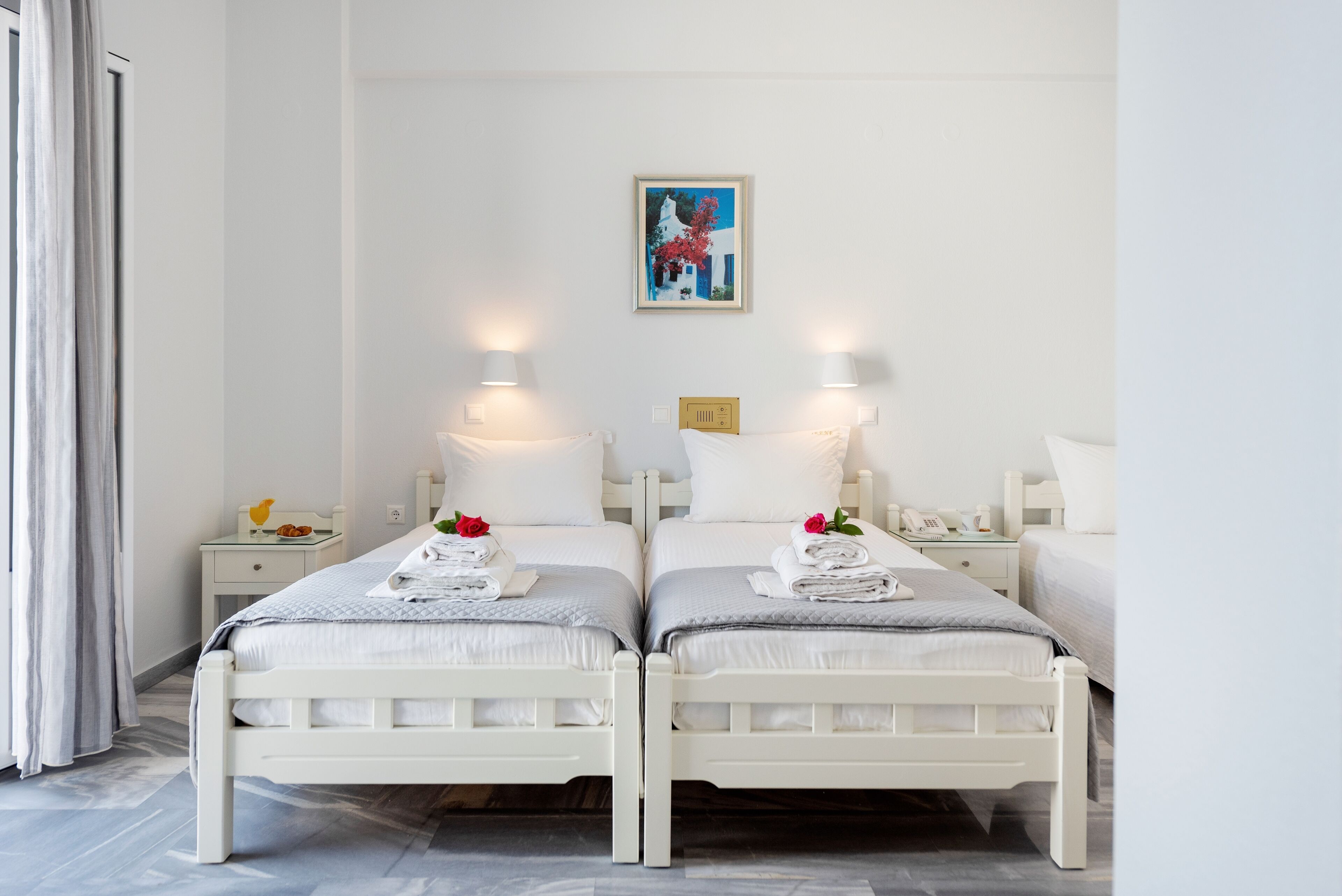Una camera d'hotel con due letti singoli, ognuno con un cuscino e un asciugamano piegato. Sopra i letti, sulla parete, c'è un quadro.
