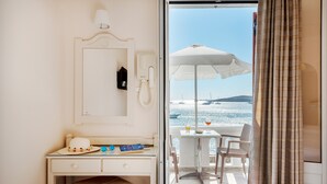 Ein Hotelzimmer mit Schreibtisch, Stuhl und Blick auf das Meer durch eine Glasdoor.