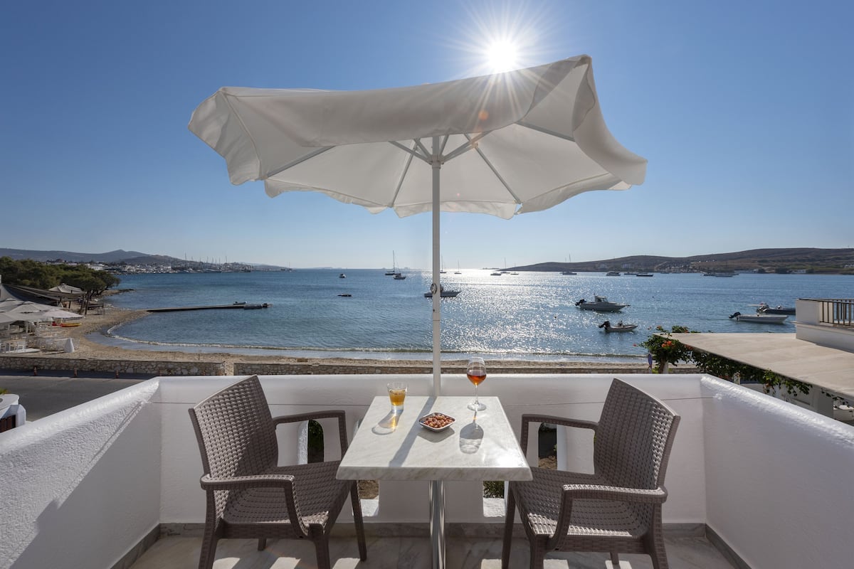 Un balcón con mesa y sillas, con vistas a una zona costera con barcos y un cielo despejado.