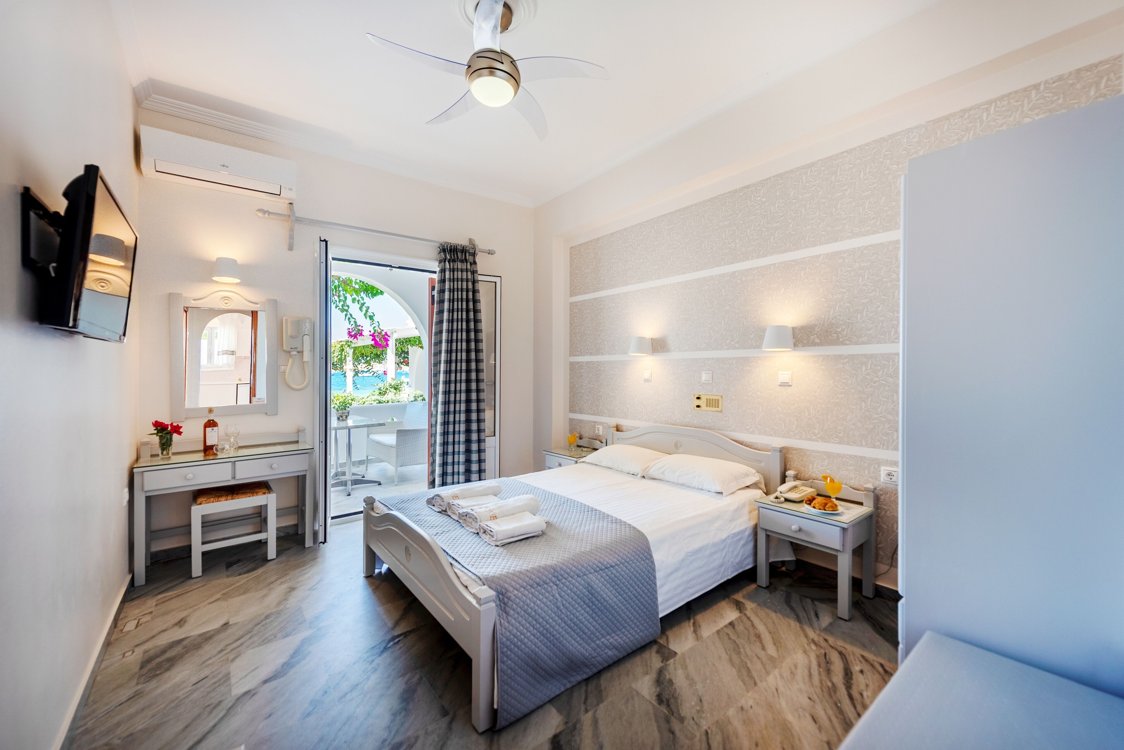A modern hotel room with a bed, bedside table, nightstand, and a desk with a chair.