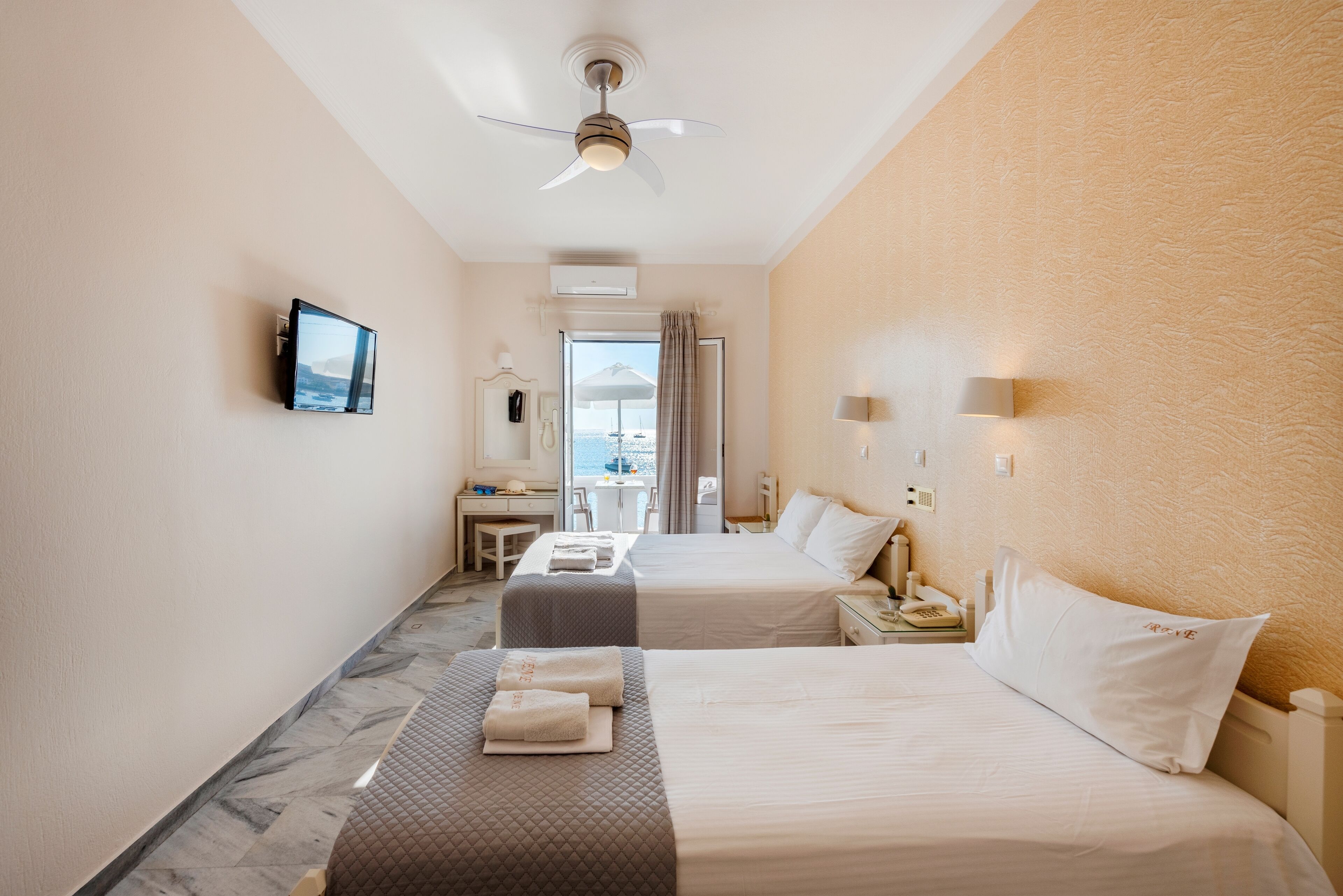 Habitación de hotel con dos camas, un escritorio, un televisor y vista al mar.