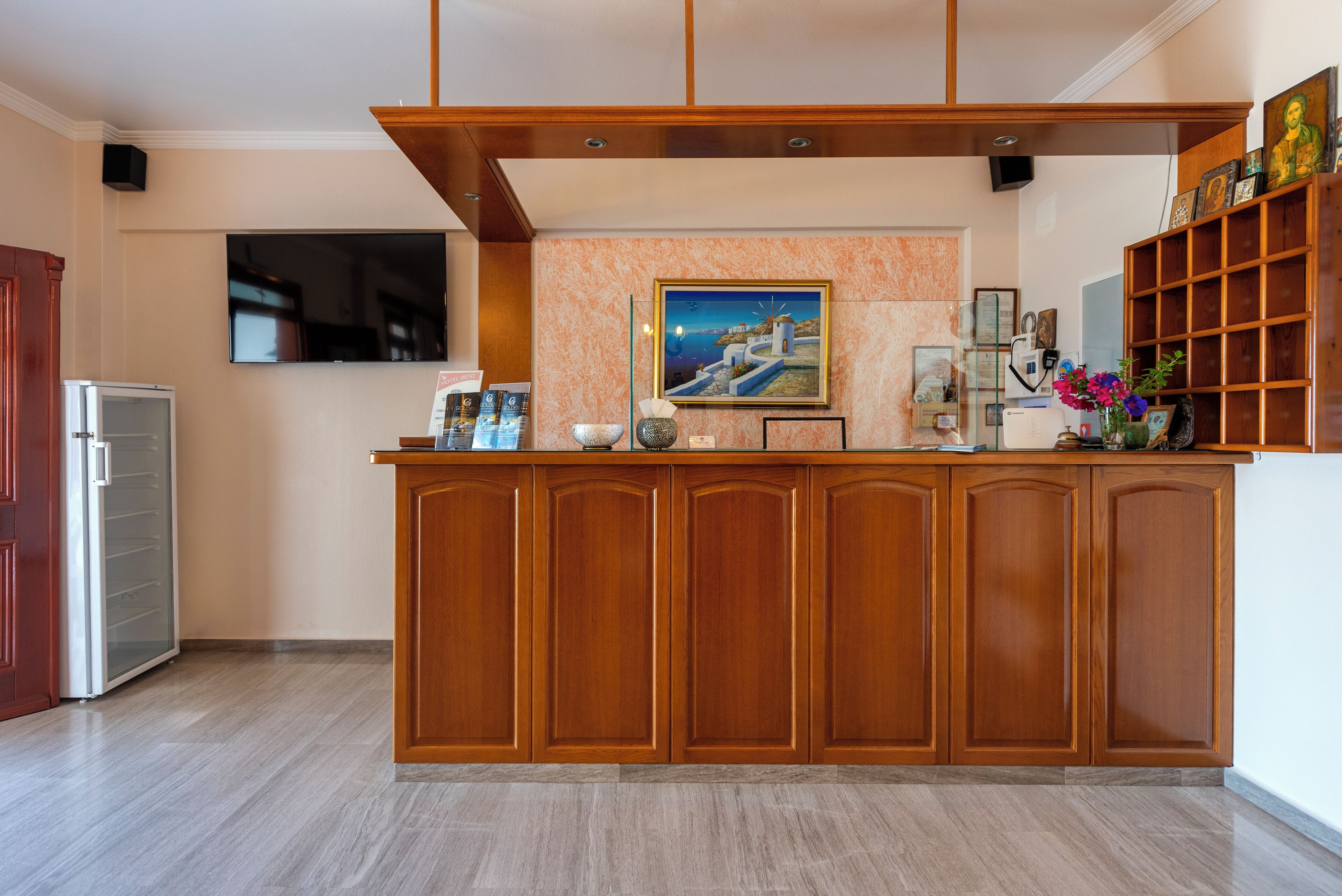 Un espace d’accueil avec un comptoir en bois, un téléviseur fixé au mur et une étagère où sont exposés des photos encadrées et des objets décoratifs.