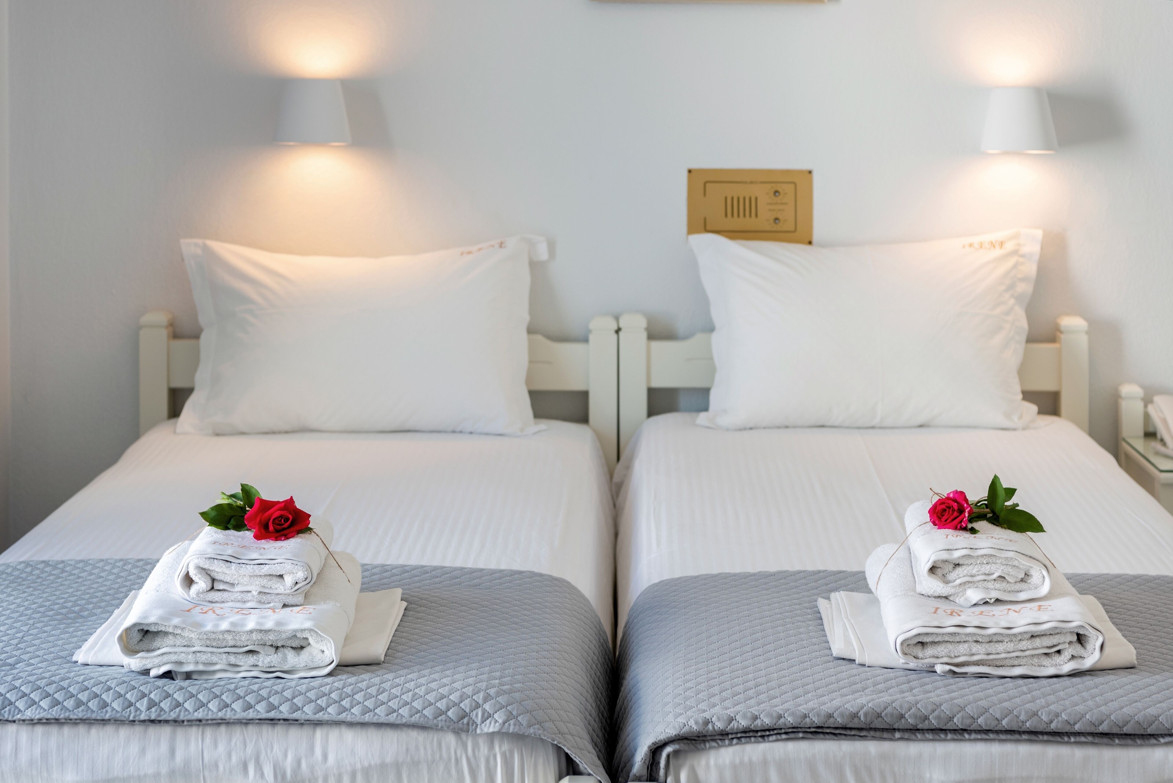 Deux lits jumeaux avec du linge de lit blanc et des oreillers, chacun agrémenté d’une serviette roulée et d’une rose.