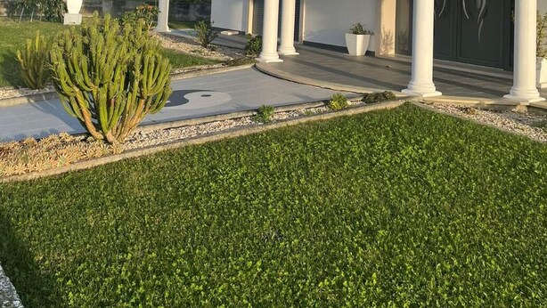 Une maison à deux étages, avec une façade blanche, un toit recouvert de tuiles rouges et un porche abrité doté de colonnes.