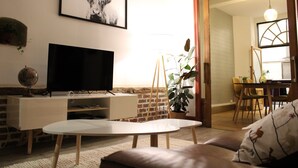 A living room with a flat-screen TV, a round table, a sofa, and a dining area with chairs and a table.