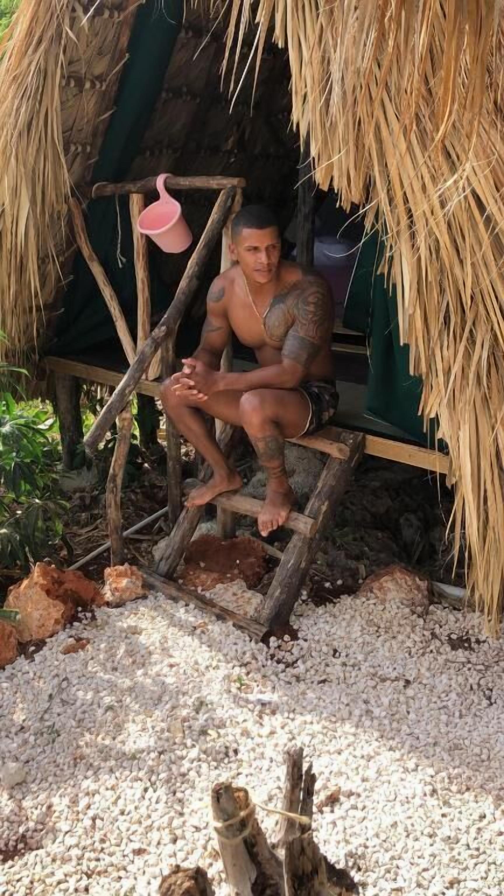 A person sitting on a wooden bench under a thatched roof structure.