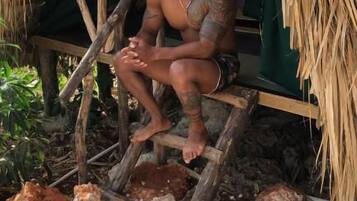 A person sitting on a wooden bench under a thatched roof structure.