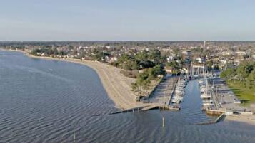 An aerial view of a coastal marina with docks and boats, surrounded by residential buildings and greenery.