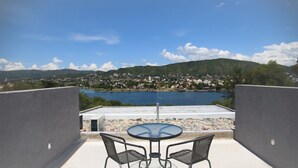 A balcony with a table and chairs overlooking a lake and a town. - Domus Lake Resort (Villa Carlos Paz)
