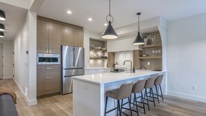 A modern kitchen with a central island, stainless steel appliances, and bar stools. - 5 bedroom home with direct ski access, sauna, private laundry and garage (Silver Star Mountain)