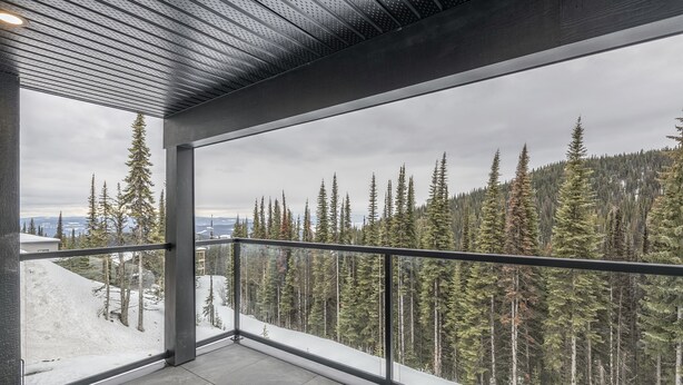 A balcony with a metal railing overlooking a forested area with snow on the ground. - 5 bedroom home with direct ski access, sauna, private laundry and garage (Silver Star Mountain)