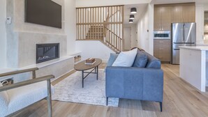 A modern living room with a fireplace, a sofa, and a staircase leading to a kitchen area. - 5 bedroom home with direct ski access, sauna, private laundry and garage (Silver Star Mountain)