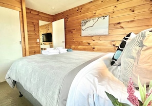 Un dormitorio con un panel de madera en la pared, una cama con colcha gris estampada y un cuadro de una rama de árbol.