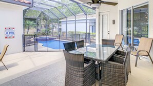En glasindrammet patio med pool, fletmøbler og en loftventilator.