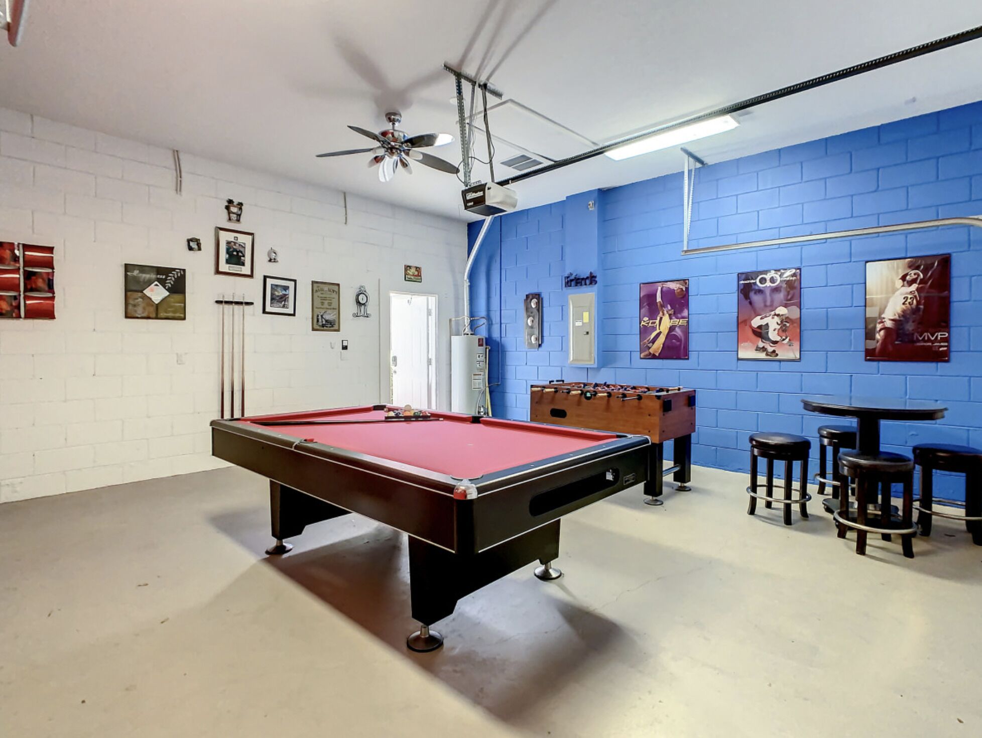 A billiards table, a foosball table, and a ceiling fan in a room with blue walls and white brick accents.