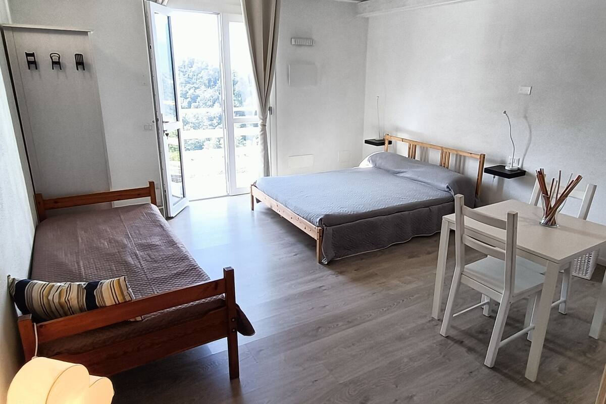 A bedroom with a bed, a desk, and a chair. There is a window with a view of trees.