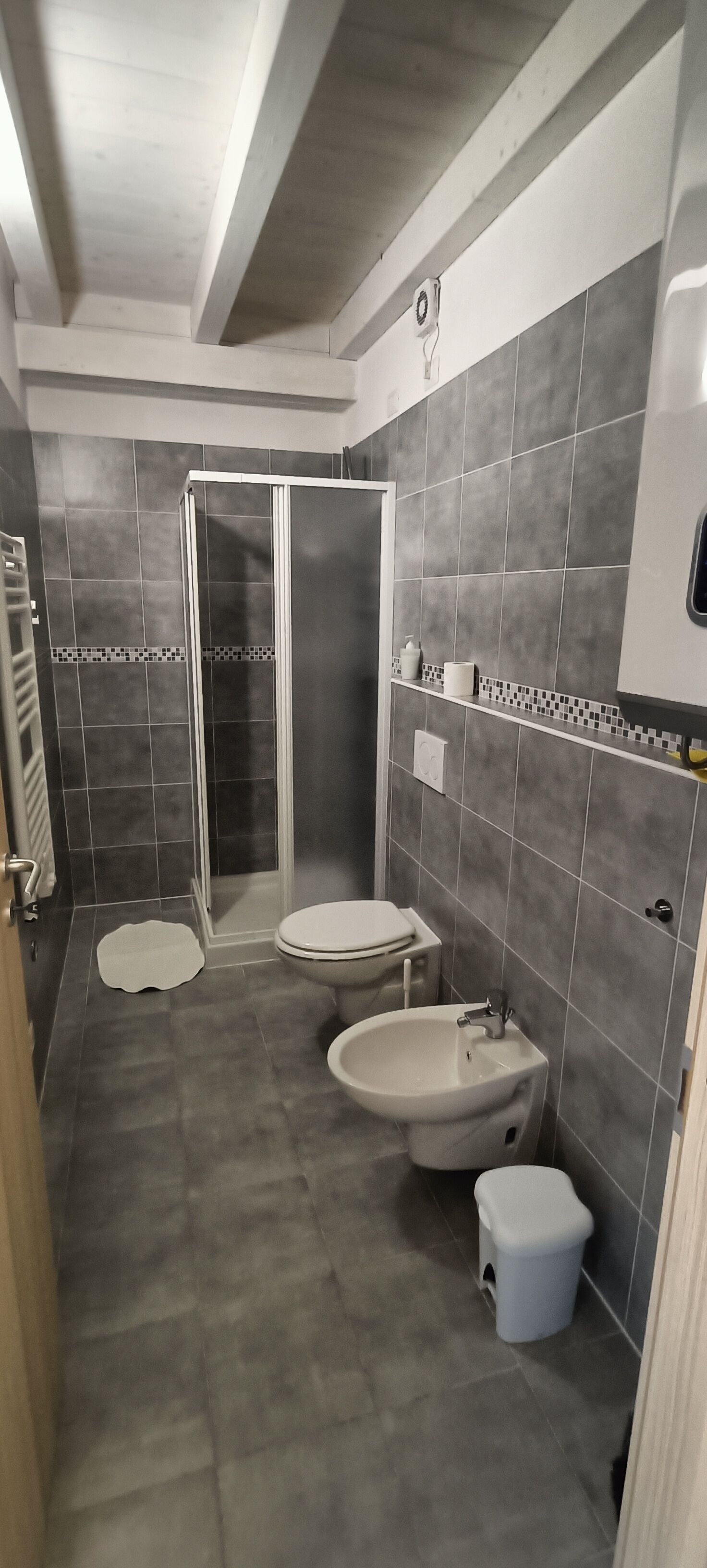 Un bagno con doccia, wc, bidet e lavandino, tutti con accessori bianchi e piastrelle grigie.