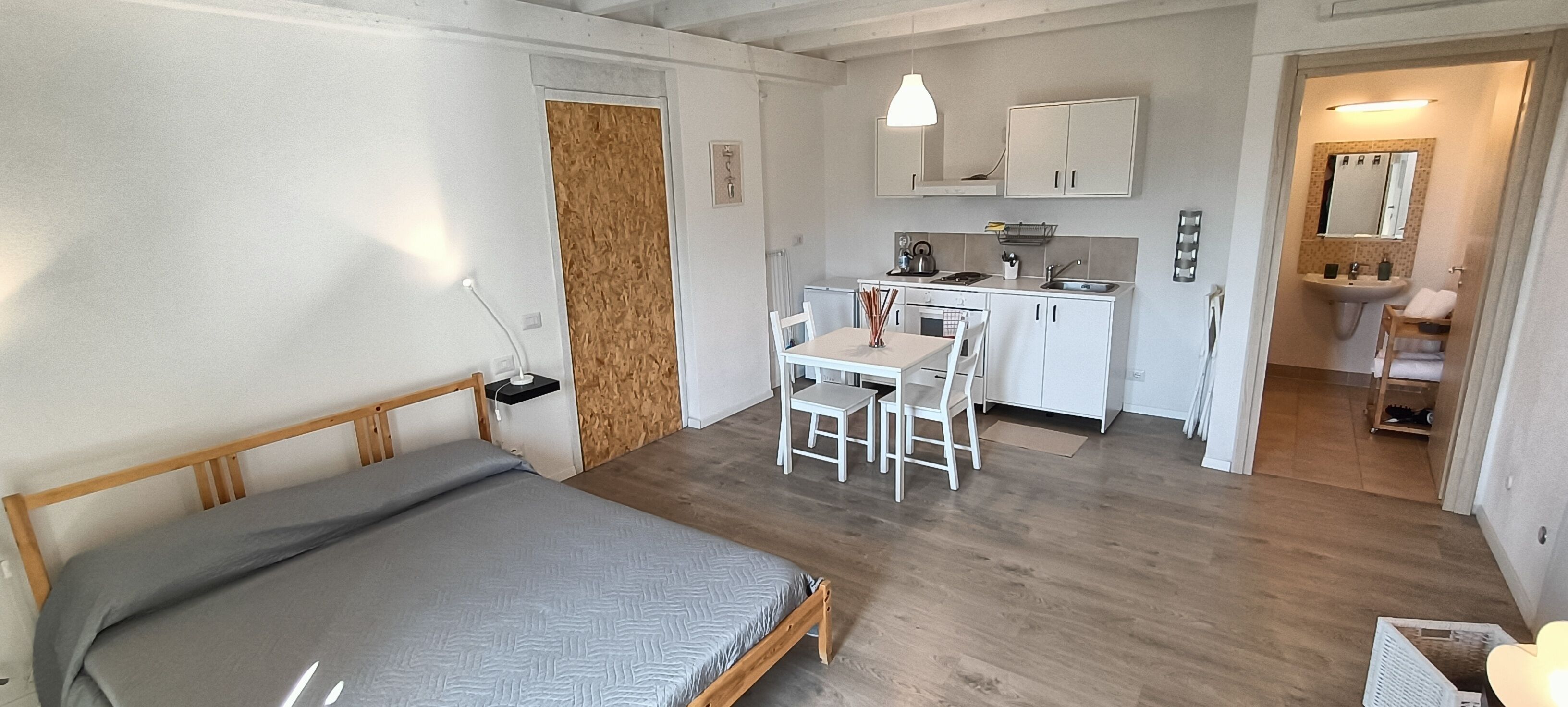 A compact bedroom with a bed, a small desk, and a kitchenette.