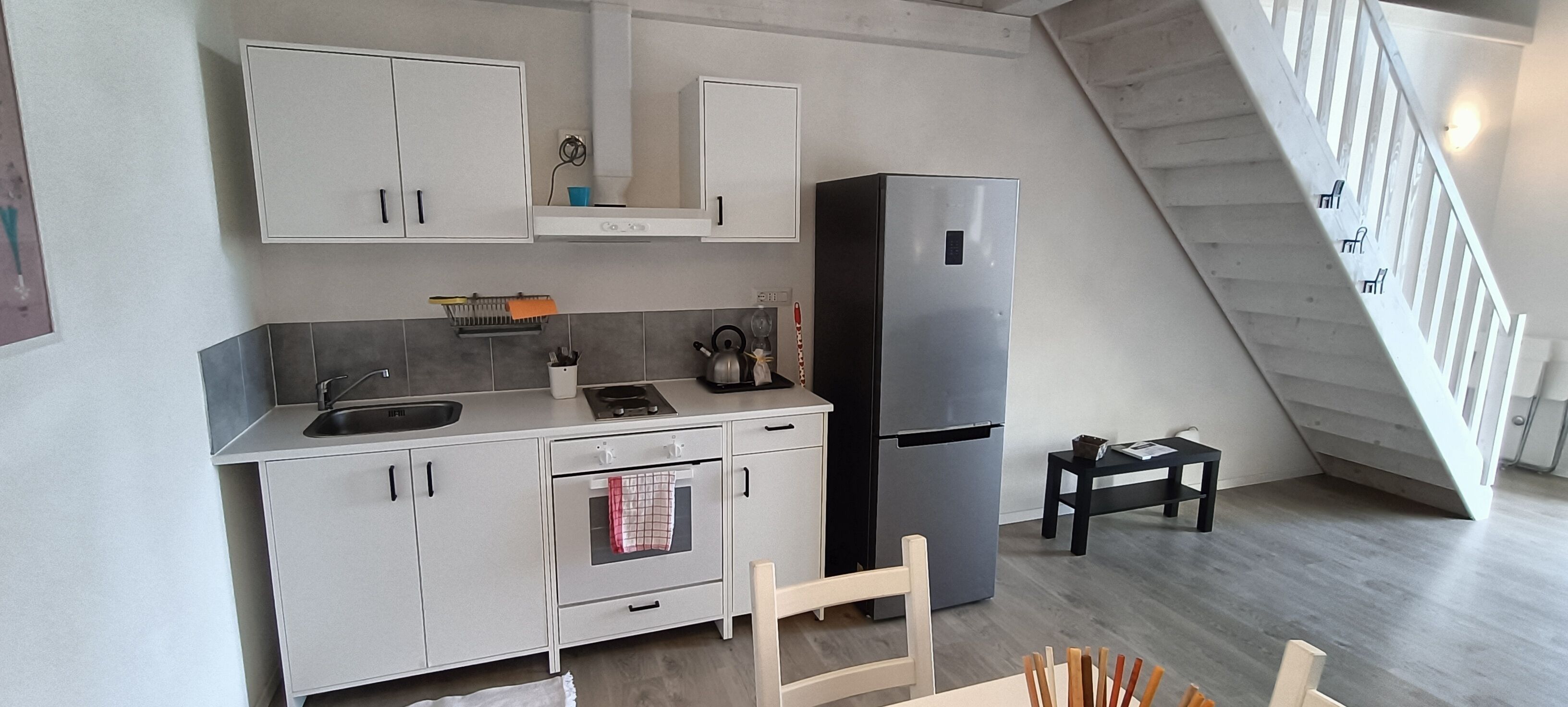 Une cuisine moderne dotée d’un four encastré, d’un réfrigérateur en acier inoxydable et d’un coin repas avec une chaise et une table en bois.