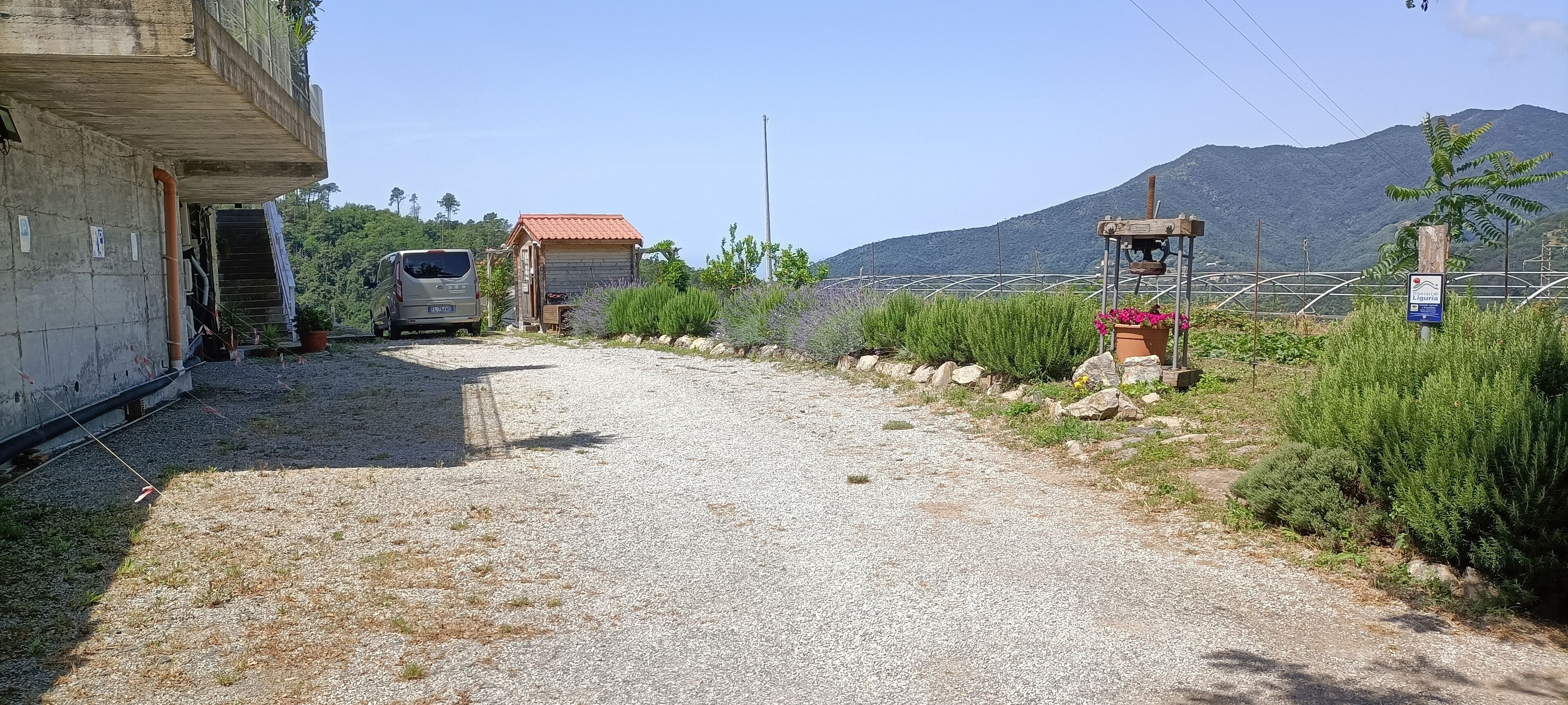 A gravel path leading to a building with a red roof, a parked van, and a signboard.