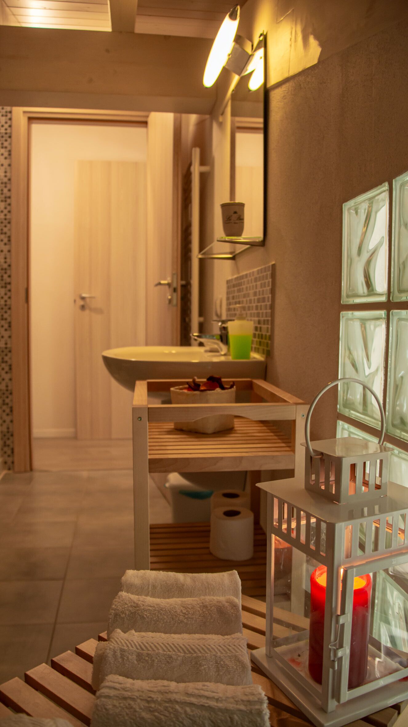 Een badkamer met een houten wastafelmeubel, een wastafel, een spiegel, een handdoekrek en een decoratieve kaarshouder.