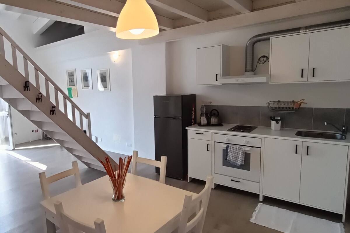 A modern kitchen with white cabinets, a black refrigerator, and a dining area with a table and chairs.