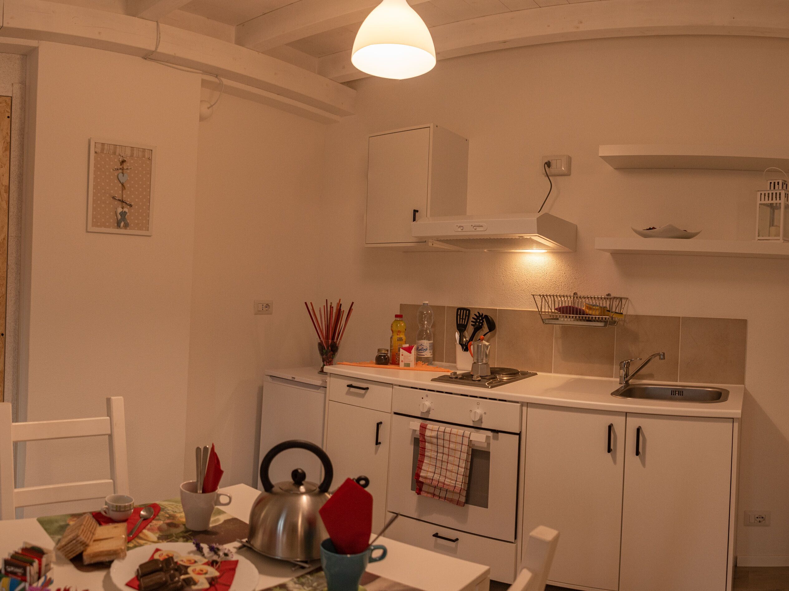 Una cocina con armarios blancos, una estufa, un fregadero y una lámpara colgante.