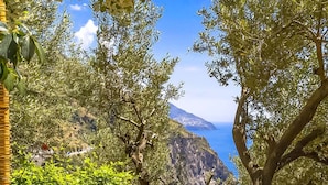 A stone wall with a stone lantern, overlooking a coastal landscape with trees and a view of the sea. - Villa Vanessa in Positano (Vico Equense)