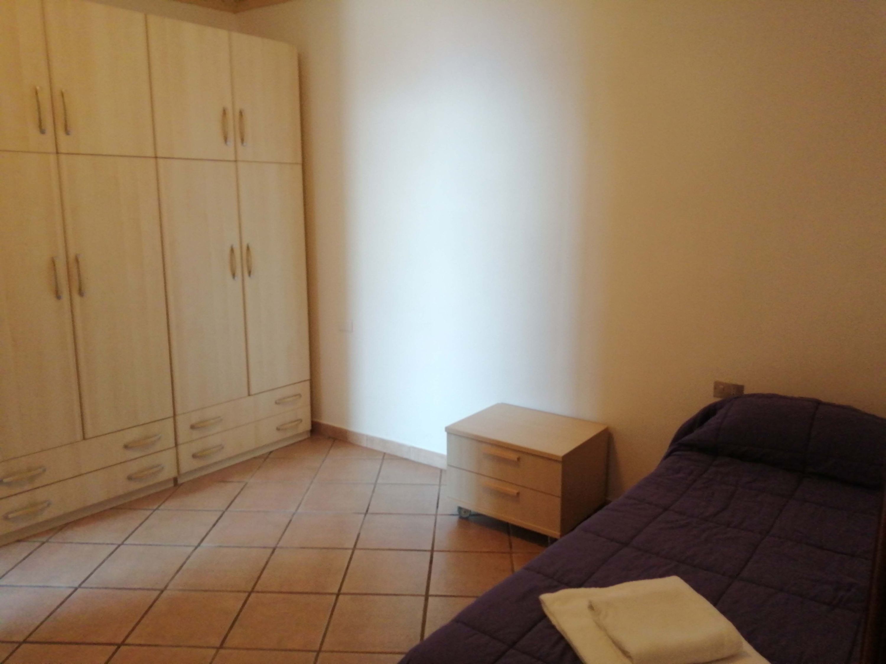 A bedroom with a bed, a small bedside table, and a wardrobe.