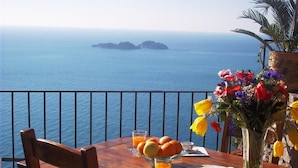 A wooden table with breakfast items, a vase of flowers, and a view of the sea. - Villa Vanessa in Positano (Vico Equense)
