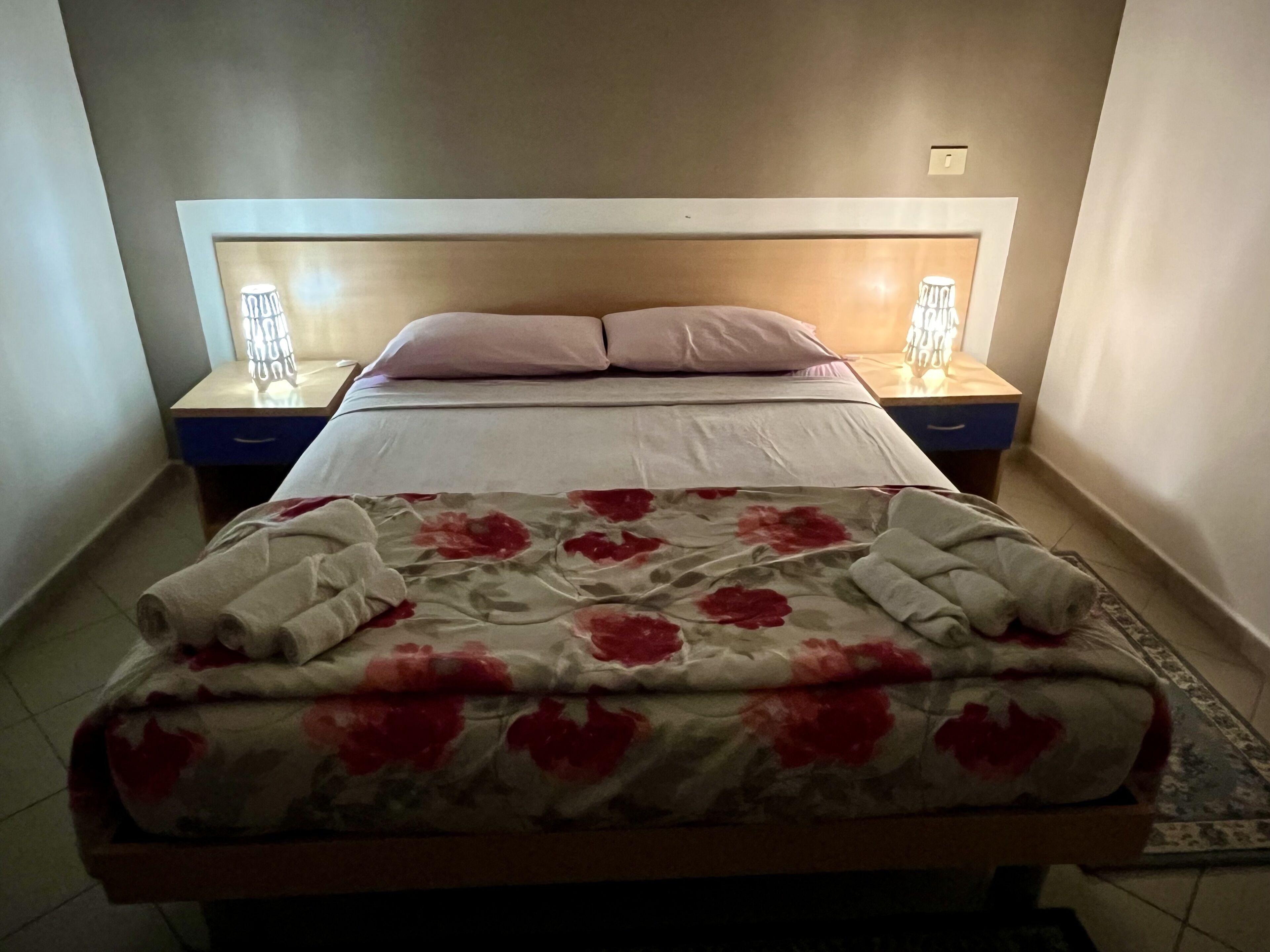 Un llit ben arropat amb un edredó floral i dos almoiners, flanquejat per taules de nit amb làmpades.
