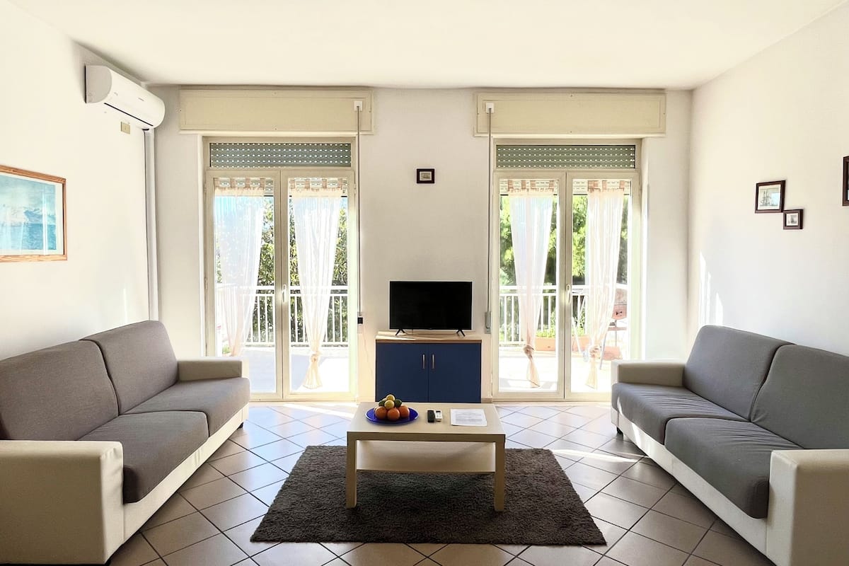 A living room with two sofas, a coffee table, a TV, and a sliding glass door leading to an outdoor area.