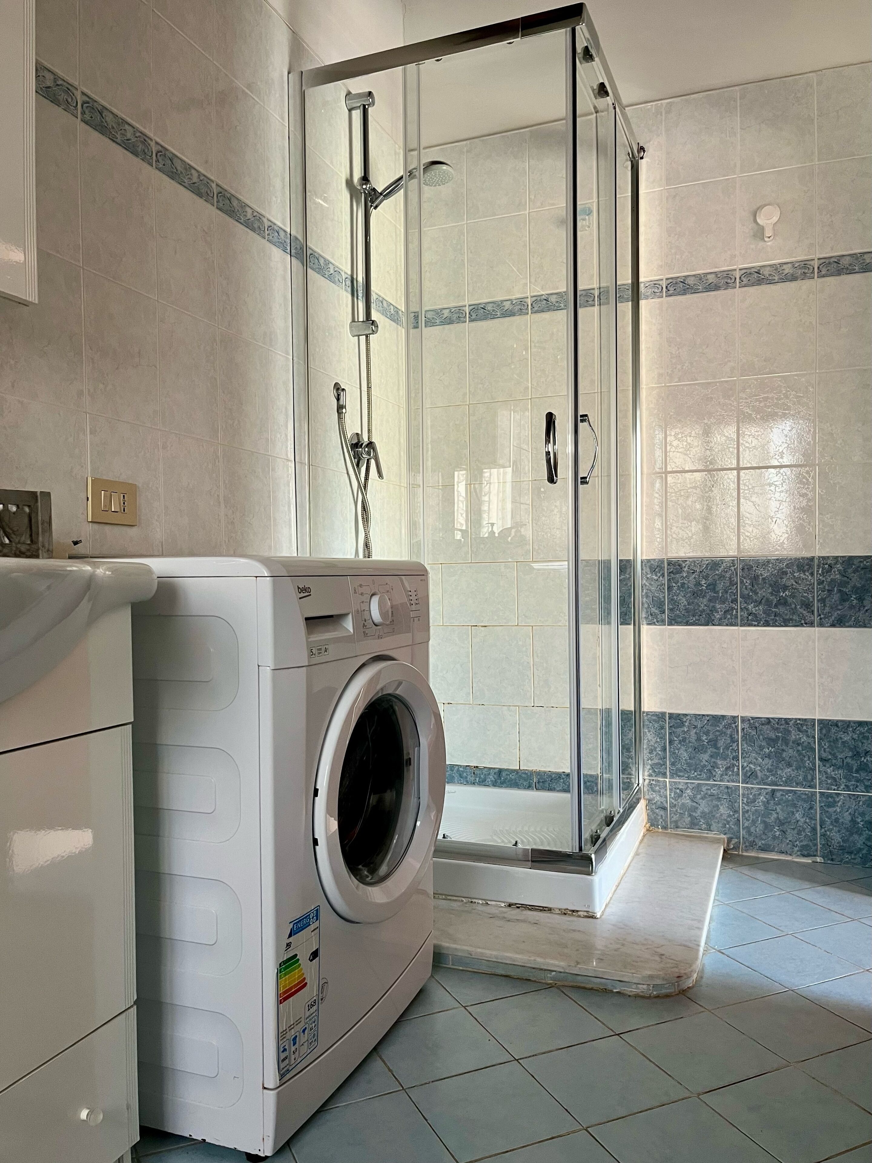 A modern bathroom with a glass-enclosed shower, a washing machine, and tiled walls.