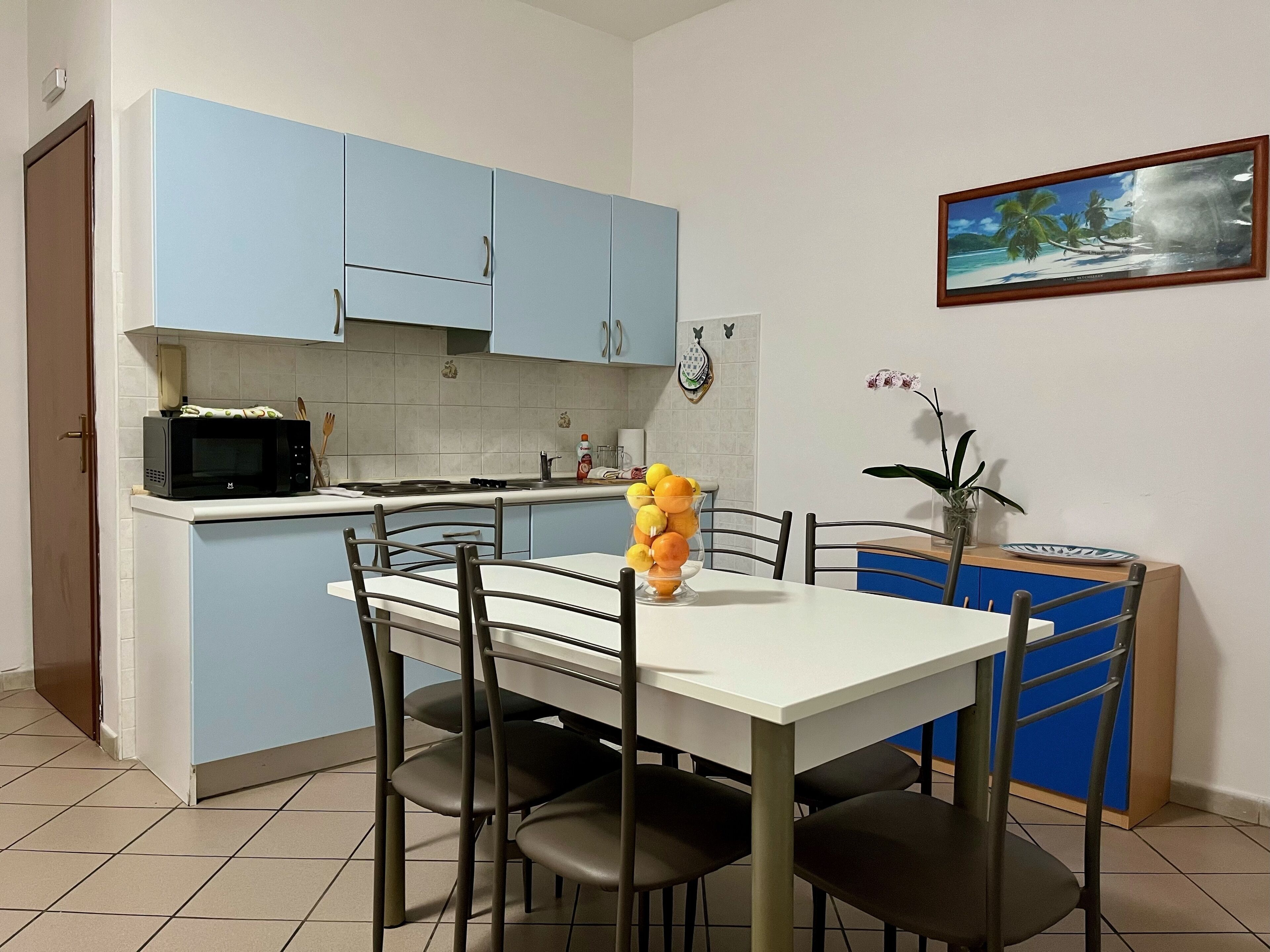 A compact kitchen with blue cabinets, a microwave, and a dining table with chairs.