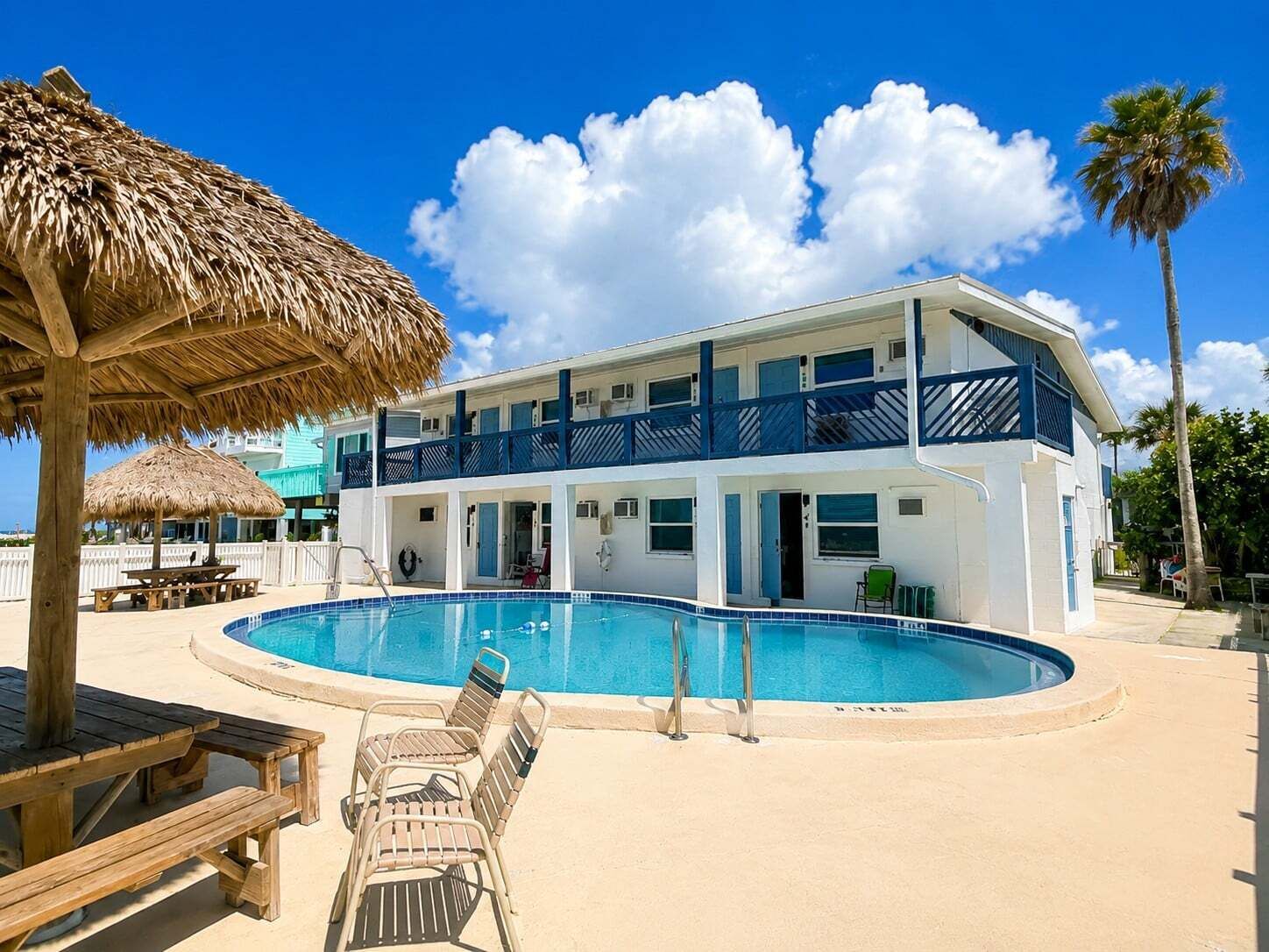 A two-story building with a swimming pool, a thatched umbrella, and a beach chair.
