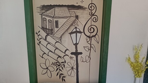 En pænt redt seng med mønstrede puder, et dekorativt kunstværk på væggen og en vase med blomster.