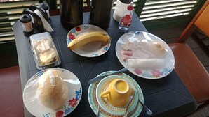 Et bord dækket med en banan, en tallerken med kød, en tallerken med brød, et glas juice og en termokande.