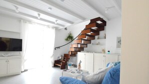 Un salon avec un canapé blanc, une table basse, un téléviseur, un escalier avec des marches en bois et un meuble blanc.