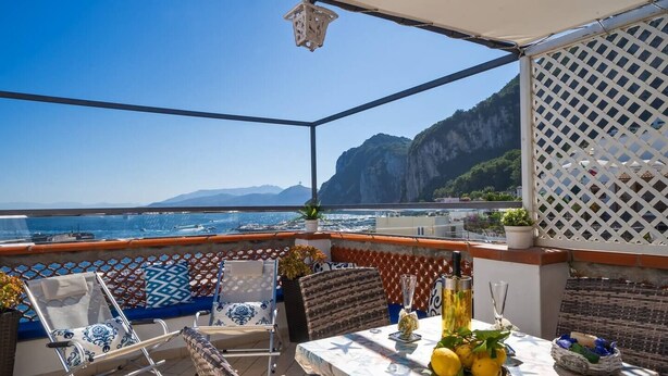A terrace with a view of the sea and mountains, furnished with chairs and a table with lemons and a bottle. - Donna Rosa Capri - Charming House by the Sea (Capri)