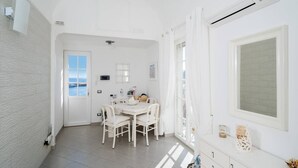 A bright, white room with a dining area, a large window with curtains, and a view of the sea. - Donna Rosa Capri - Charming House by the Sea (Capri)